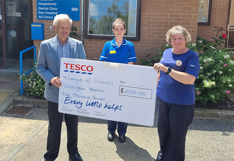 A man and two women holding a very large cheque with Tesco branding